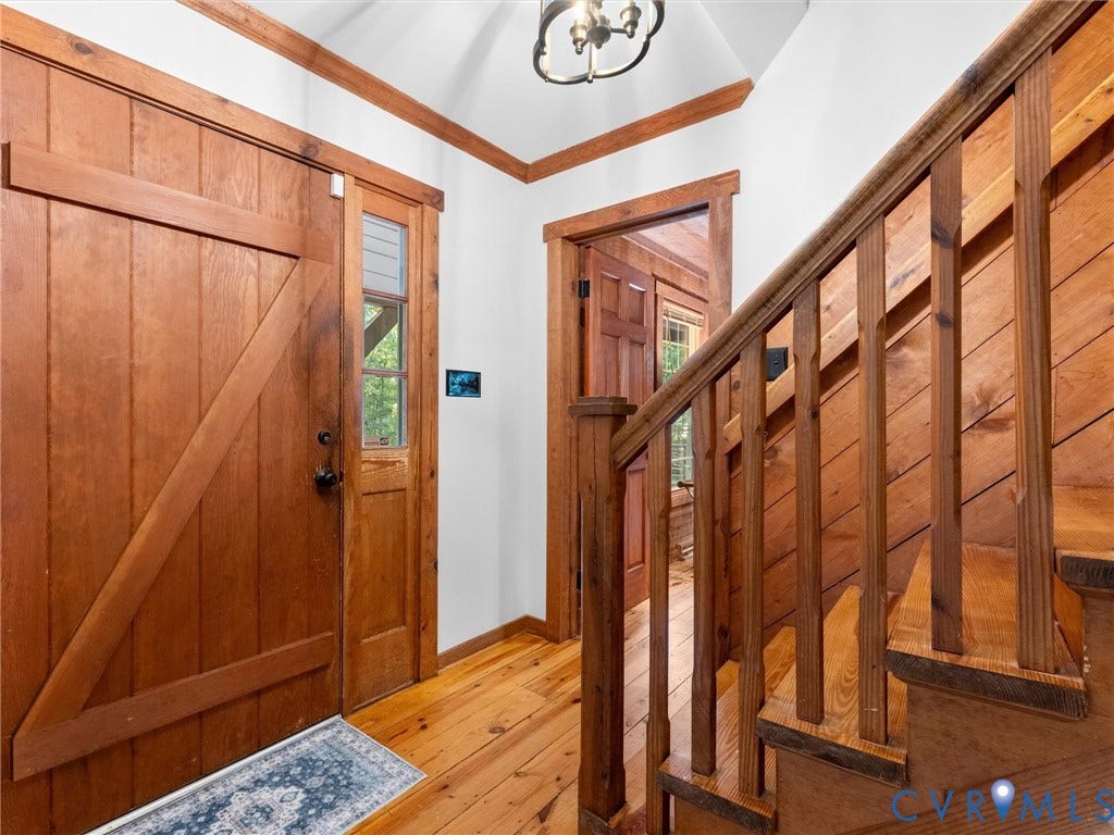 3801 Old River Trail, Powhatan, VA 23139 Foyer featuring a wood-plank door with cross-buck detailing, wood-finish flooring, a wood staircase with vertical balusters, wood door casings, and a multi-arm ceiling fixture
