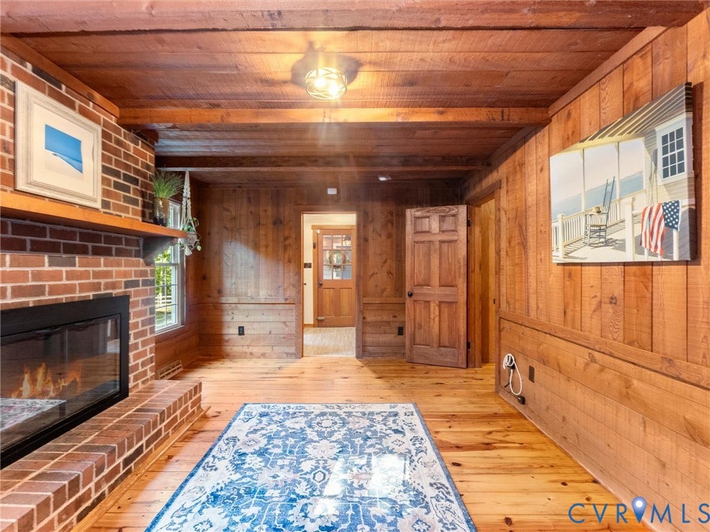 3801 Old River Trail, Powhatan, VA 23139 Interior space featuring wood-paneled walls and ceiling, exposed wooden ceiling beams, brick fireplace surround, and wood flooring