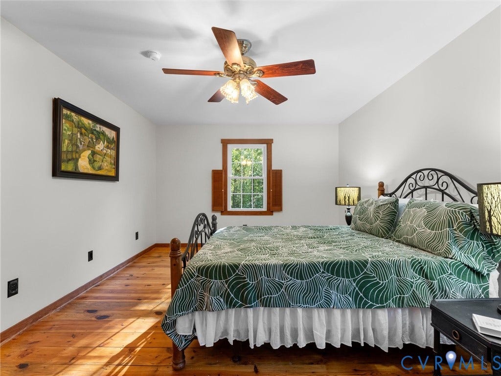 3801 Old River Trail, Powhatan, VA 23139 Natural finish plank wood flooring, center-mounted ceiling fan with light fixture, window with wood-trim casing, and attached wooden shutter accents