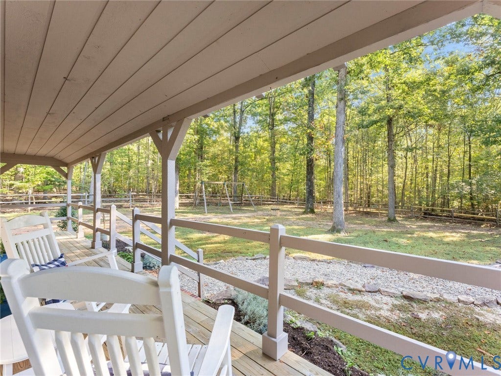 3801 Old River Trail, Powhatan, VA 23139 Covered porch featuring a wood-plank deck, rail fencing, and expansive outdoor space with mature trees and stone-bordered ground cover
