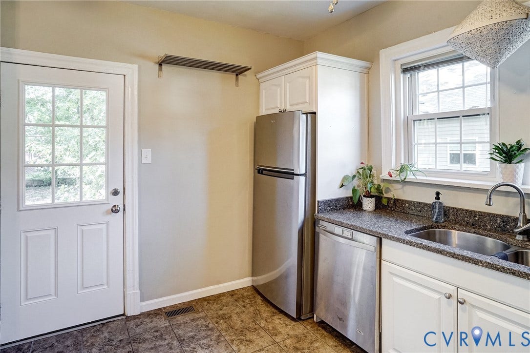 White paneled exterior door with divided light window, tiled flooring, stainless steel refrigerator, stainless steel dishwasher, and a double basin sink with a window above