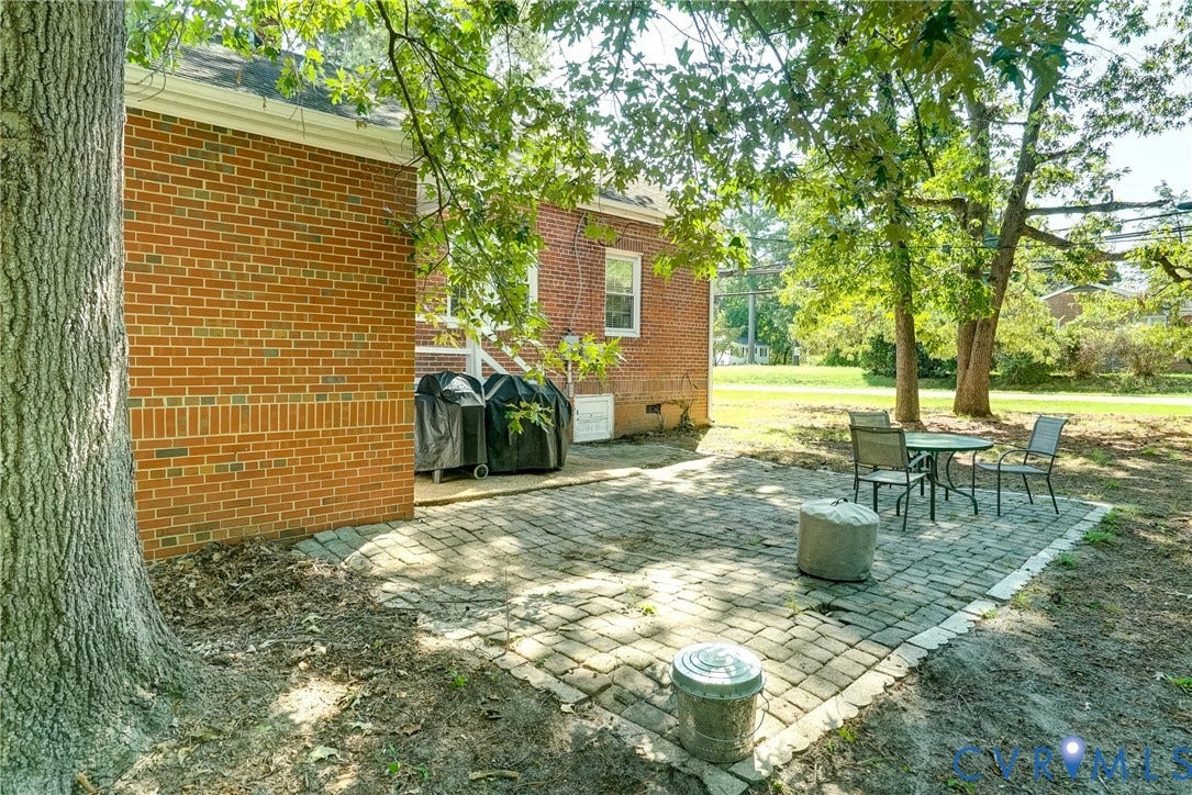 Brick exterior with white trim, paver patio, and mature trees