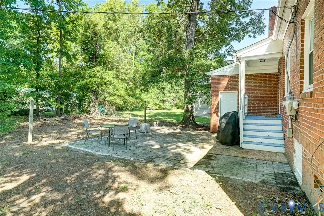 Red brick exterior with white trim, covered porch entry, paver patio, and mature tree landscaping