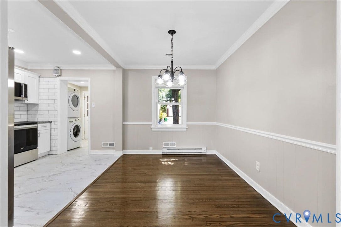 1215 Starling Drive, Henrico, VA 23229 Hardwood flooring, crown molding, chair rail, and wainscoting details, with an open transition to the kitchen featuring white shaker cabinetry and stainless steel appliances