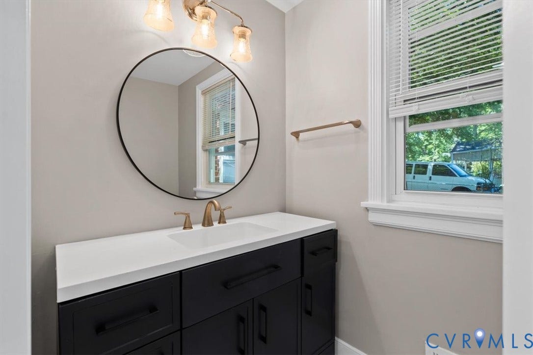 1215 Starling Drive, Henrico, VA 23229 Vanity with a white countertop and dark cabinetry, bronze-finish faucet, circular mirror, and window with blinds