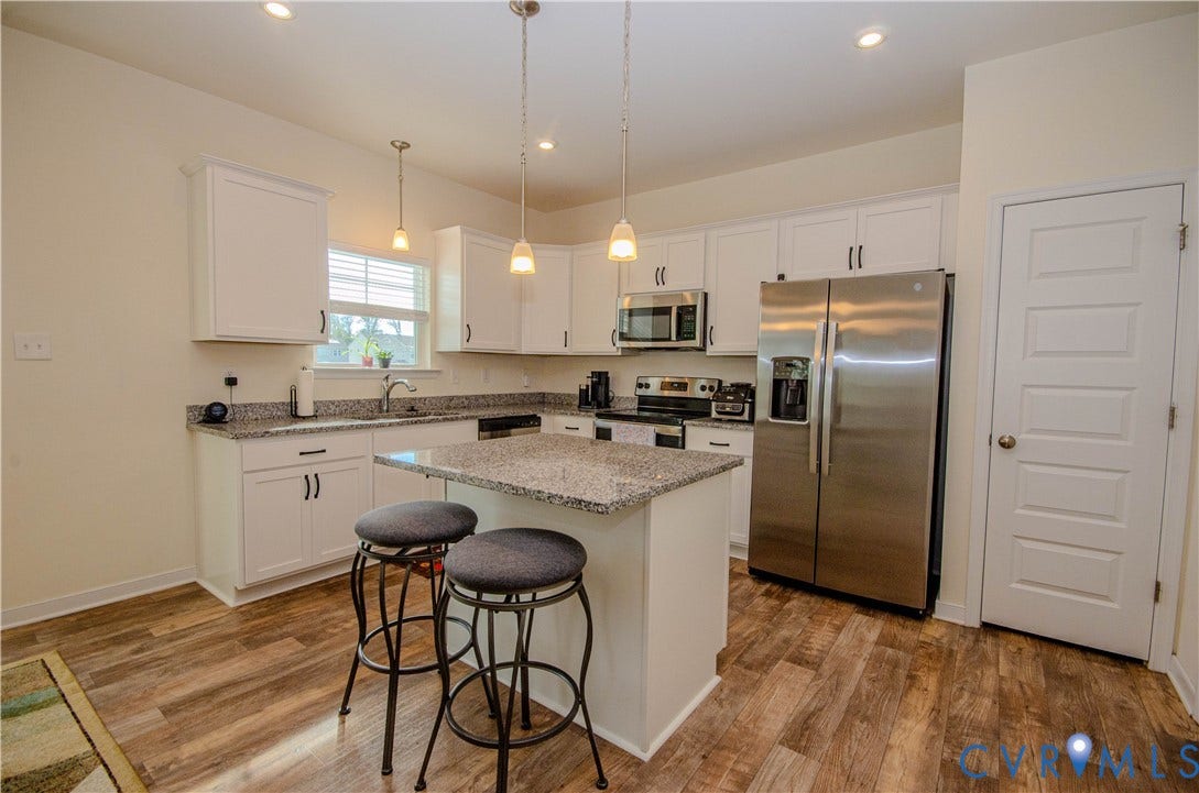 Kitchen featuring stainless steel appliances, white cabinetry, granite countertops, a kitchen island, and pendant lighting