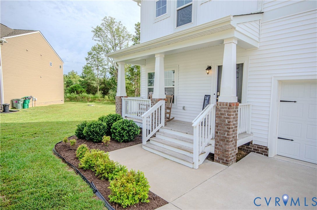 Inviting covered front porch with brick column bases, white railings, and a concrete walkway
