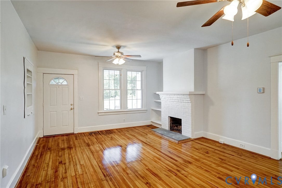 10024 Washington Road, Richmond, VA 23060 Hardwood flooring throughout, a white brick fireplace with hearth, multiple windows, built-in shelving, and two ceiling fans with lighting