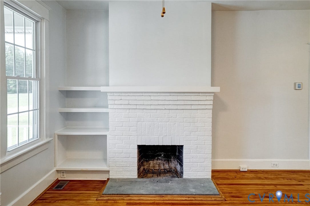 10024 Washington Road, Richmond, VA 23060 Brick fireplace with a stone hearth, built-in shelving, wood-finish flooring, and a large window