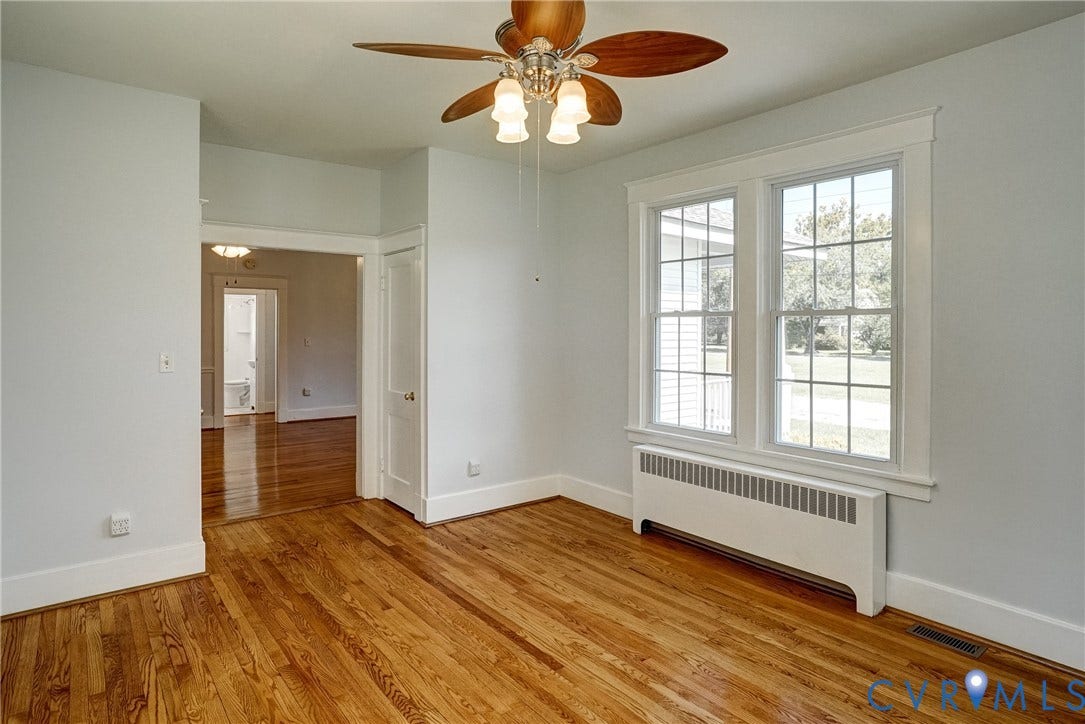 10024 Washington Road, Richmond, VA 23060 Hardwood flooring throughout, double-hung windows with white trim, ceiling fan with light fixture, and a white baseboard radiator
