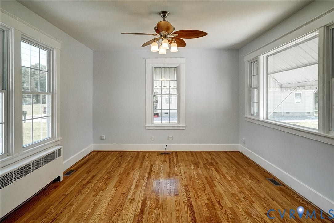 10024 Washington Road, Richmond, VA 23060 Hardwood flooring, multiple windows with white trim, ceiling fan with integrated lighting, and a baseboard heating unit