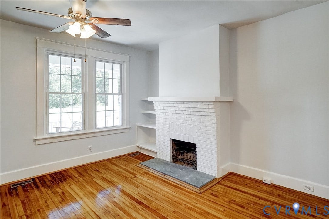 10024 Washington Road, Richmond, VA 23060 Hardwood flooring, painted brick fireplace with stone hearth, built-in shelving, dual windows with grilles, and a ceiling fan with integrated lighting