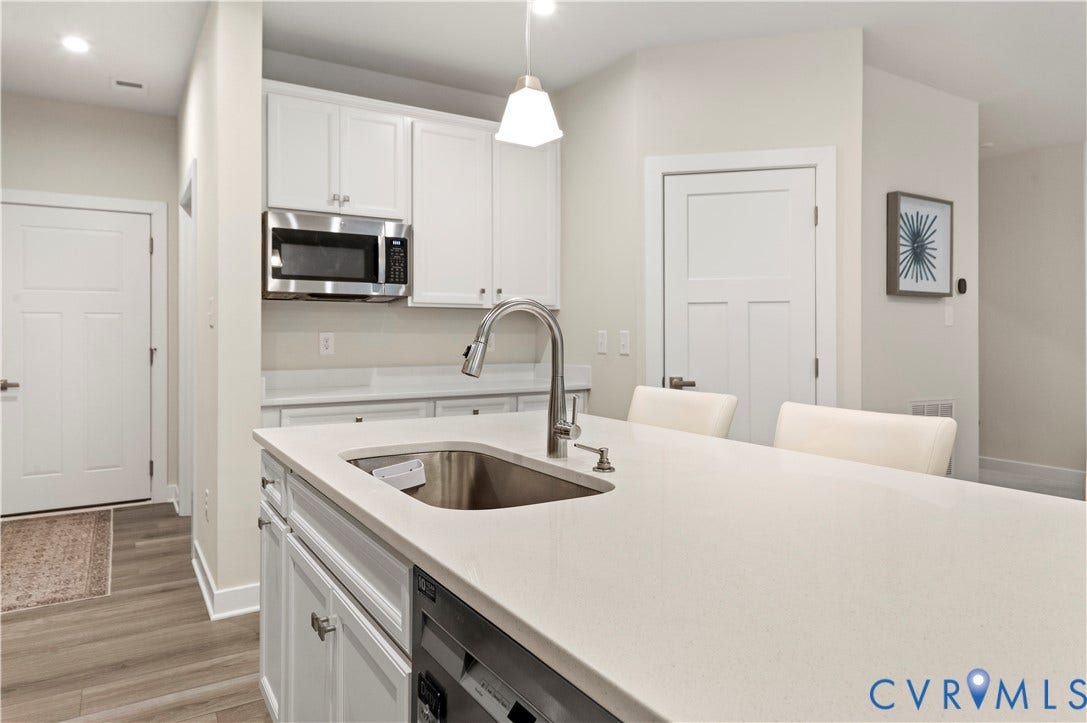 4837 Bacova Village Trail, Glen Allen, VA 23059 Kitchen featuring a large island with an integrated sink, stainless steel microwave, white shaker-style cabinetry, and wood-finish flooring