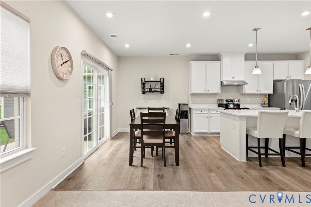 4837 Bacova Village Trail, Glen Allen, VA 23059 Open-concept kitchen and dining area featuring wood-finish flooring, white cabinetry, a kitchen island with seating, and stainless steel appliances