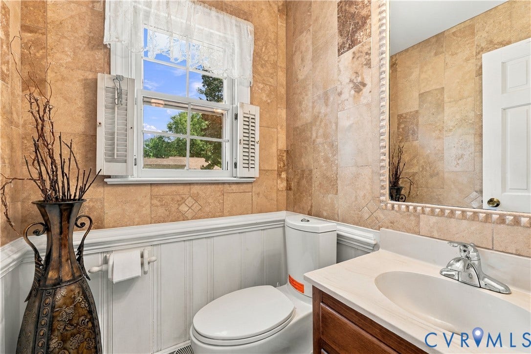 8307 Wallingford Lane, Chickahominy Bluffs, Henrico, VA 23227 Tile-finished walls with accent detailing, beadboard wainscoting, white window shutters, vanity with integrated sink, and an ornate framed mirror
