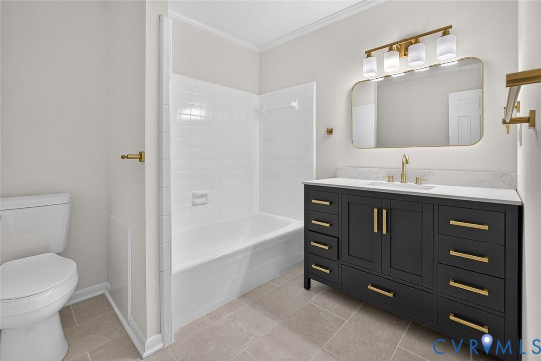 1122 Glidewell Road, Henrico, VA 23227 Dark charcoal vanity featuring brass hardware and a white countertop, rectangular vessel sink, wall-mounted brass faucet, arched vanity mirror, and neutral floor tile