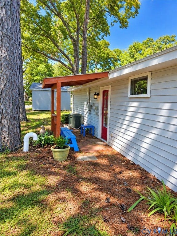 36 Beach Road, Reedville, VA 22539 Exterior featuring light grey siding, a red entry door, a covered porch entrance with a wooden pergola, and a single window with white trim