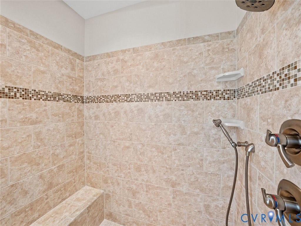 Tiled shower with a decorative mosaic band, built-in bench, handheld shower fixture, and overhead rain shower
