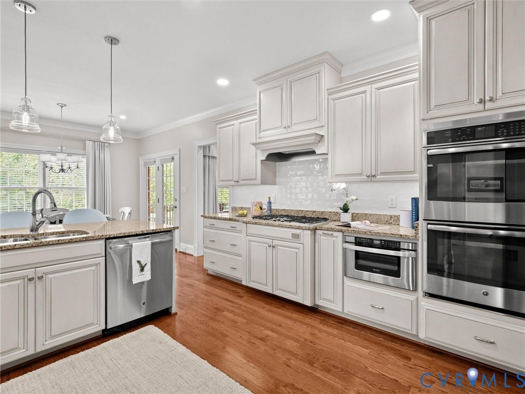 White shaker cabinetry, stainless steel appliances, granite countertops, wood-finish flooring, and pendant lighting