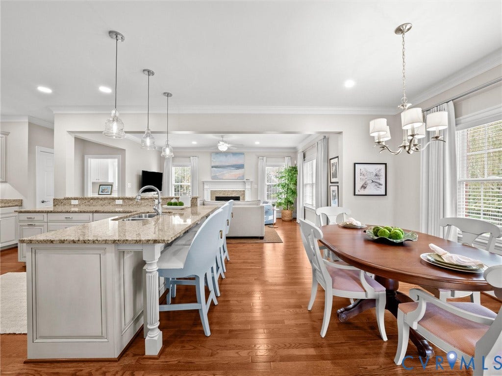 Open-concept living area with wood-finish flooring, a kitchen island with stone countertops, white shaker-style cabinetry, and pendant lighting