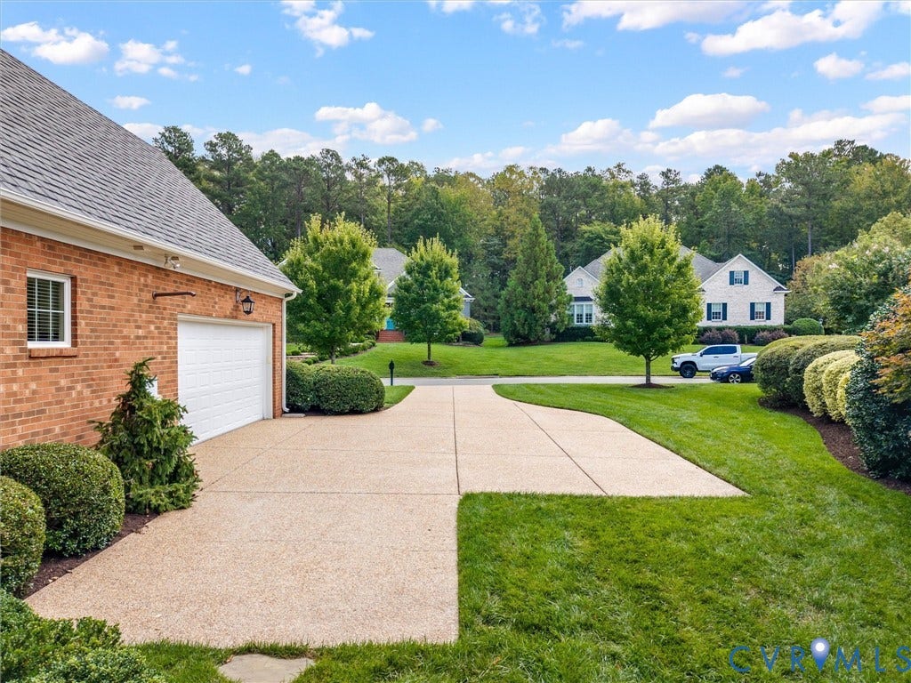 Brick exterior, attached garage, paved driveway, landscaped shrubbery, and mature trees