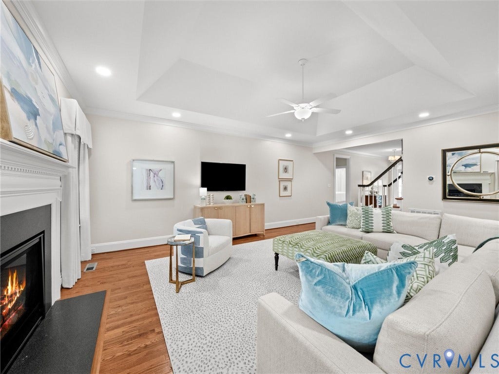 Living area featuring a tray ceiling, recessed lighting, ceiling fan, wood flooring, and a fireplace with a white mantel and black surround