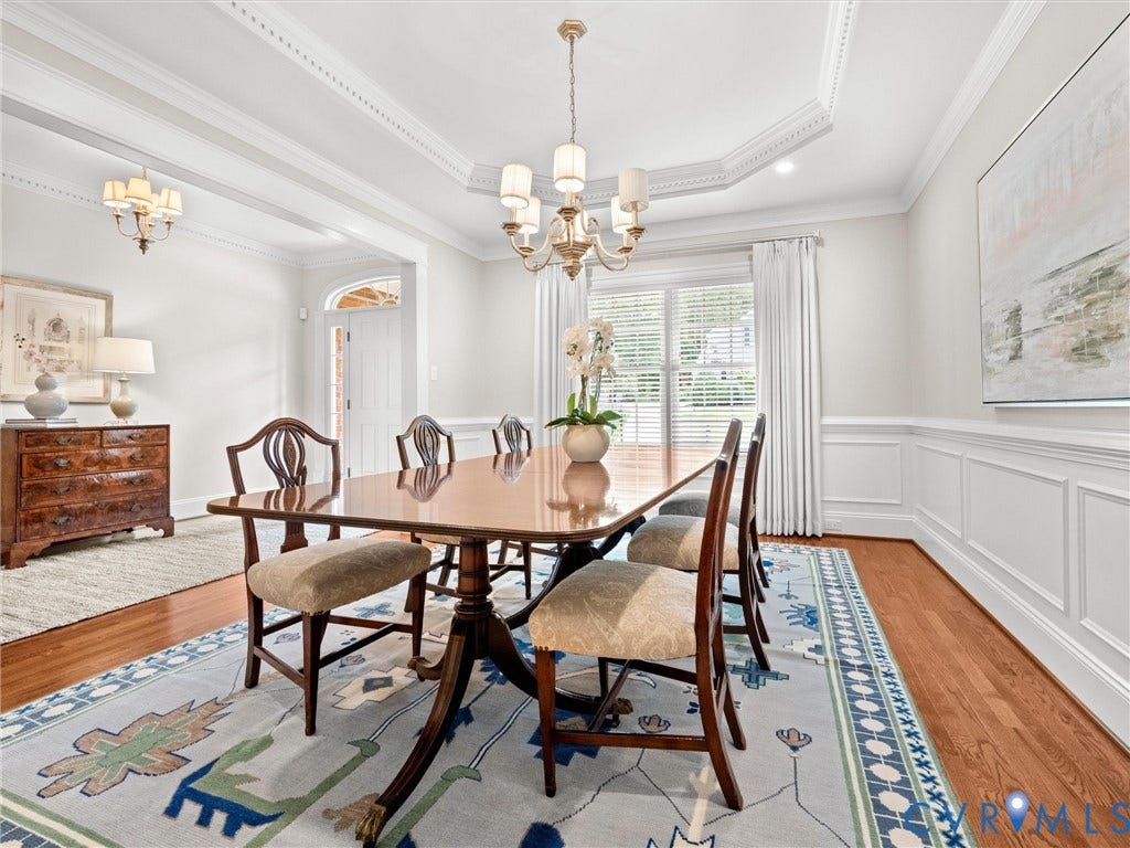 Hardwood flooring, decorative wainscoting, tray ceiling with crown molding, and a chandelier