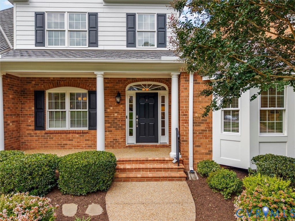 Brick and siding exterior with dark shutters, covered front porch with white columns, and a dark paneled front door with an arched transom