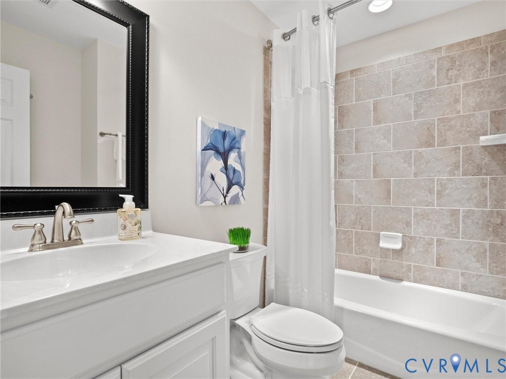 White vanity with integrated sink, brushed nickel faucet, large framed mirror, white toilet, and tiled shower surround with a built-in tub