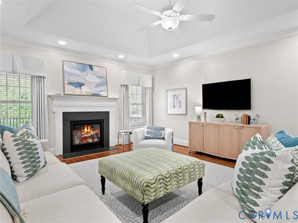 Living area featuring a tray ceiling, recessed lighting, a ceiling fan, and a fireplace with a white mantel and dark surround