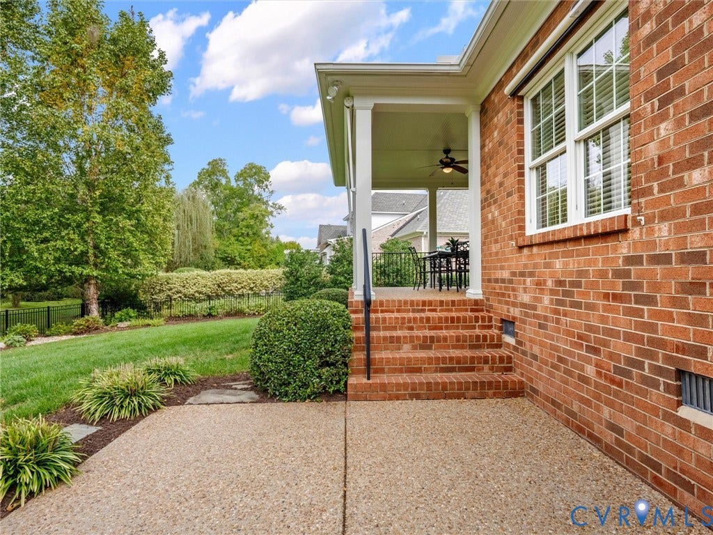 Brick exterior with white trim, covered porch with ceiling fan, brick steps with iron railing, and a gravel patio