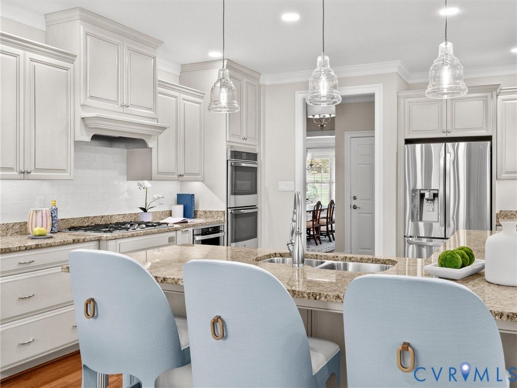 Kitchen featuring light-toned cabinetry, granite countertops, stainless steel appliances, a built-in range hood, and pendant lighting