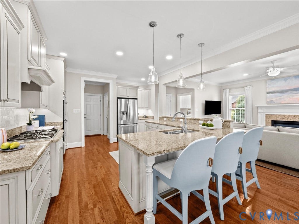 Open-concept kitchen featuring white cabinetry, granite countertops, stainless steel appliances, and a central island with a sink