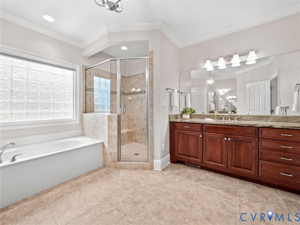 Expansive bathroom featuring a dual vanity with wood cabinetry, a built-in tub, and a glass-enclosed shower with a bench