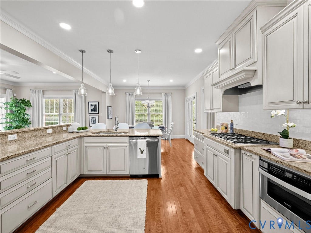 Kitchen featuring wood-finish flooring, white cabinetry, integrated stainless steel appliances, speckled stone countertops, and a subway tile backsplash