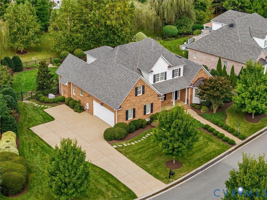 Brick facade with white siding accents and black shutters, gabled roofline, two-car garage, concrete driveway, and established landscaping