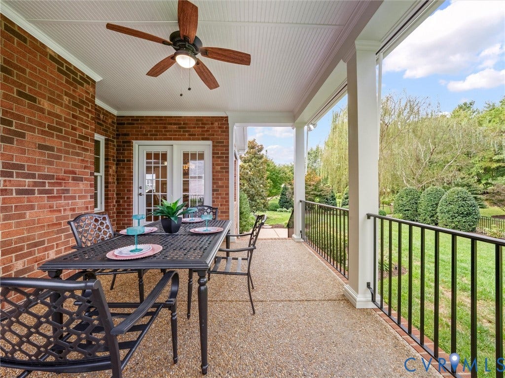 Covered patio featuring a brick exterior, exposed aggregate flooring, and white beadboard ceiling with a ceiling fan