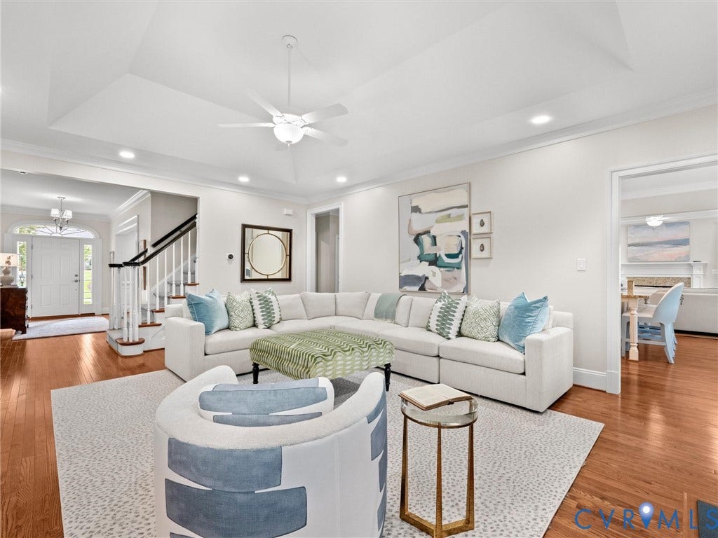 Hardwood flooring throughout, tray ceiling with recessed lighting, white wood staircase with black handrail, white paneled front door with transom window, and crown molding