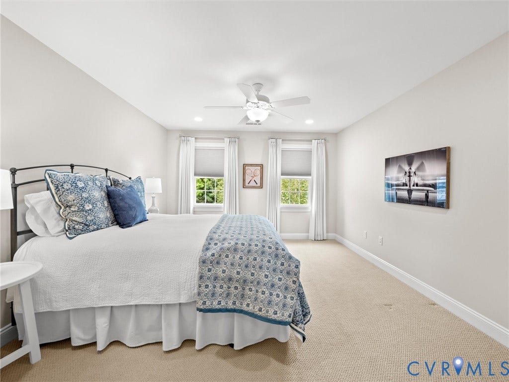 Carpeted flooring, two windows with roller shades and drapery, white ceiling fan with integrated lighting, and recessed ceiling lighting