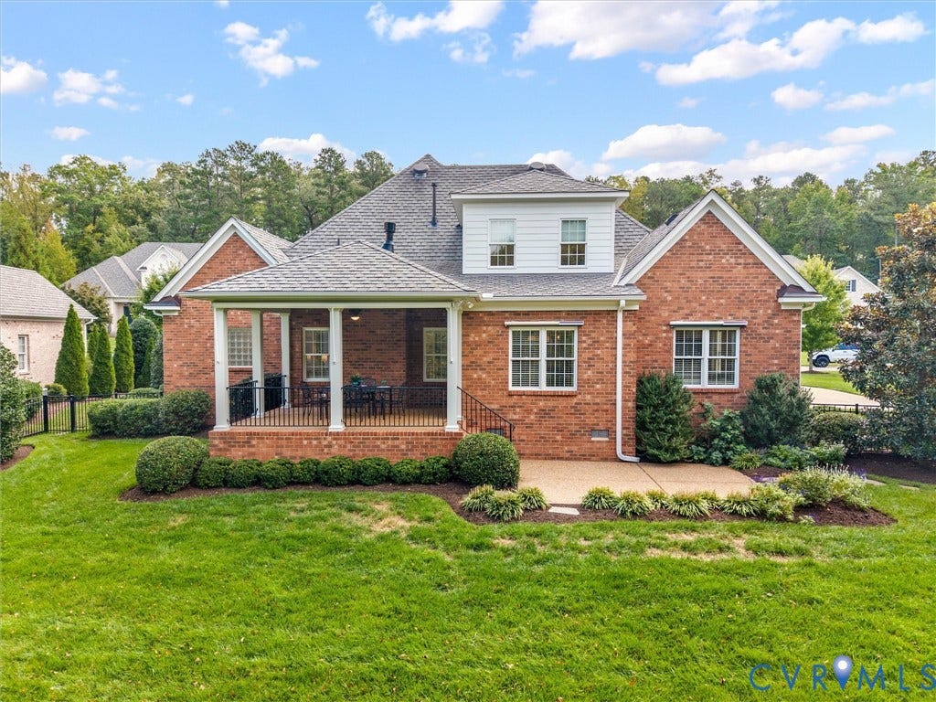 Brick exterior with a covered porch featuring white columns, a ground-level patio, and a dormer with white siding