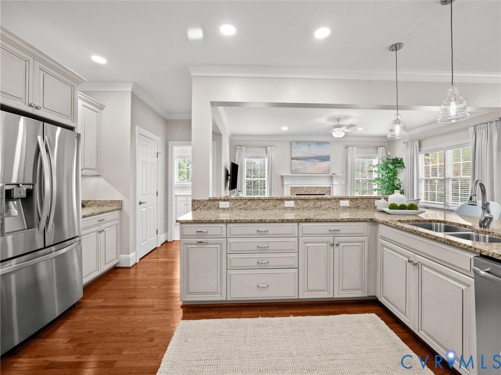Stainless steel appliances, recessed ceiling lights, wood-finish flooring, white cabinetry, and a double basin sink
