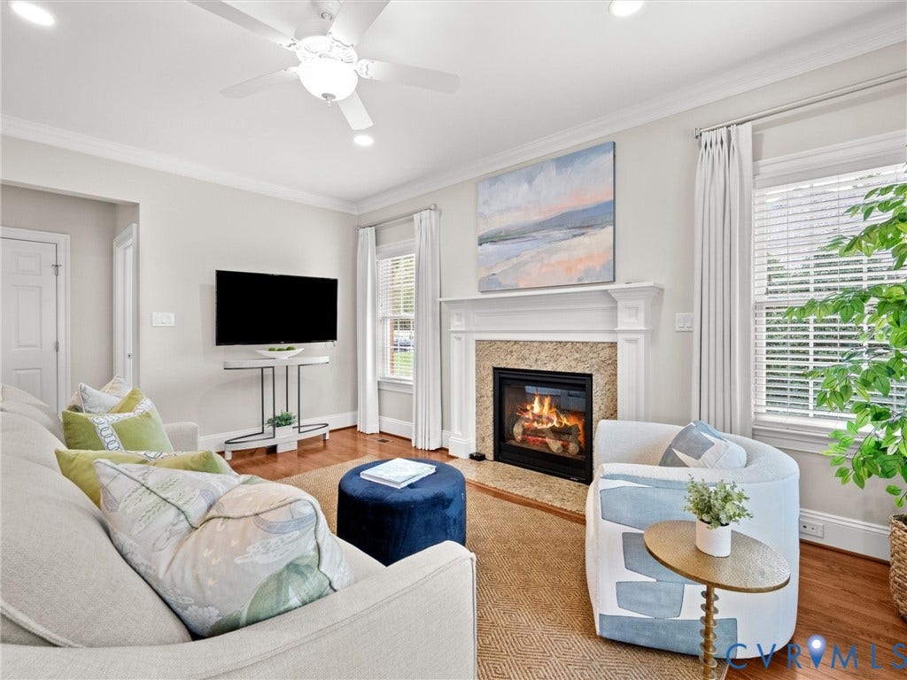 Living area featuring a fireplace with a stone surround, hardwood flooring, and a ceiling fan with integrated lighting