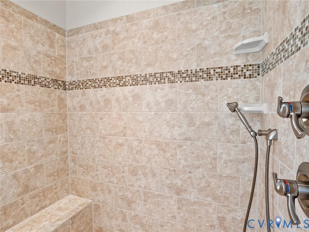 Tiled shower with a mosaic accent band, built-in bench, and handheld shower fixture