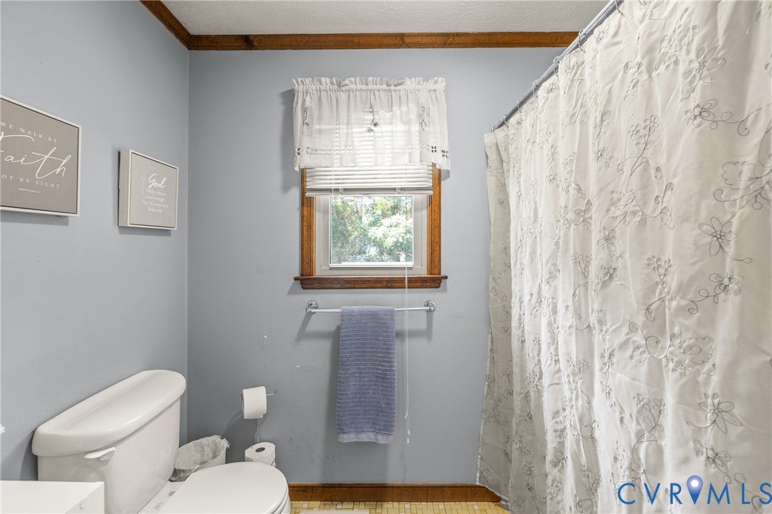 Bathroom featuring a window with wood trim, a white toilet, and a towel bar