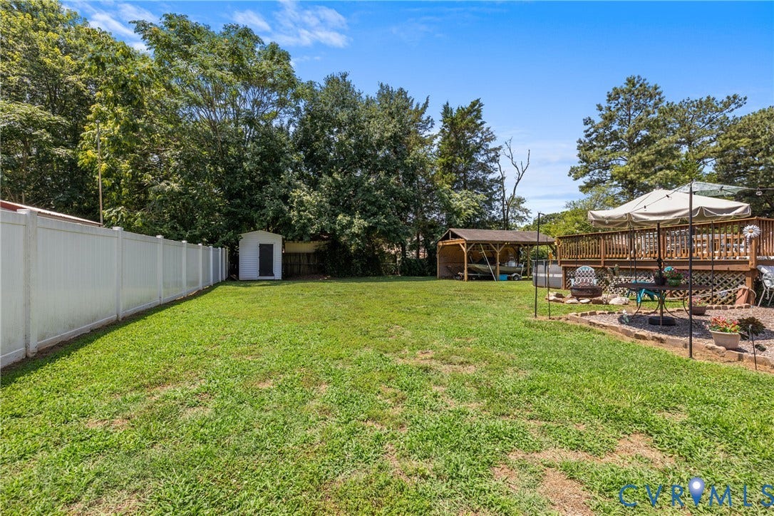 Expansive backyard featuring a white privacy fence, a storage shed, an elevated wood deck, and a detached covered structure