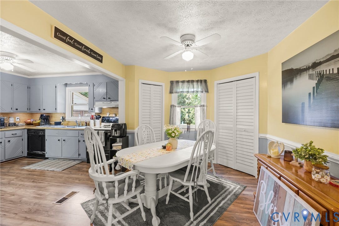 Dining area featuring wood-finish flooring, two ceiling fans with integrated lighting, and a window with natural light