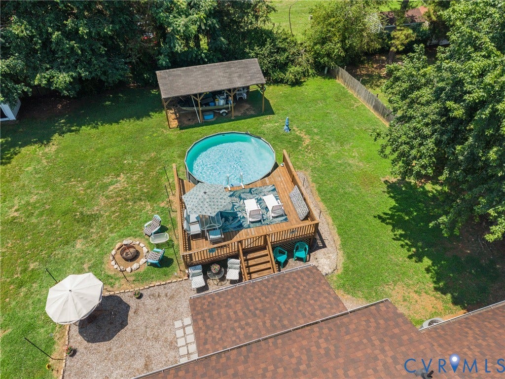 Expansive backyard featuring a manicured lawn, a raised wood deck with an above-ground pool, a covered outdoor structure, and a fire pit area