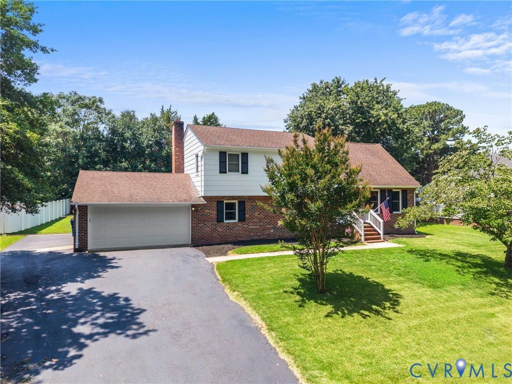 Brick and siding exterior with a pitched shingle roof, attached garage, paved driveway, and established landscaping