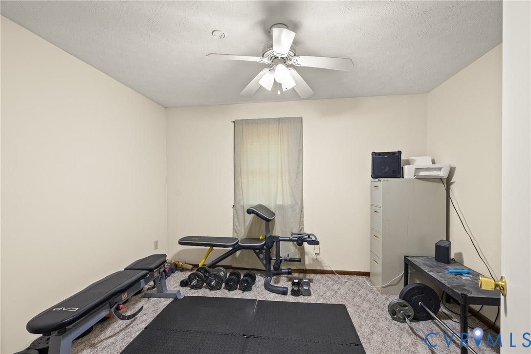 Neutral wall paint, ceiling fan with integrated lighting, window with light-filtering curtains, and carpeted flooring