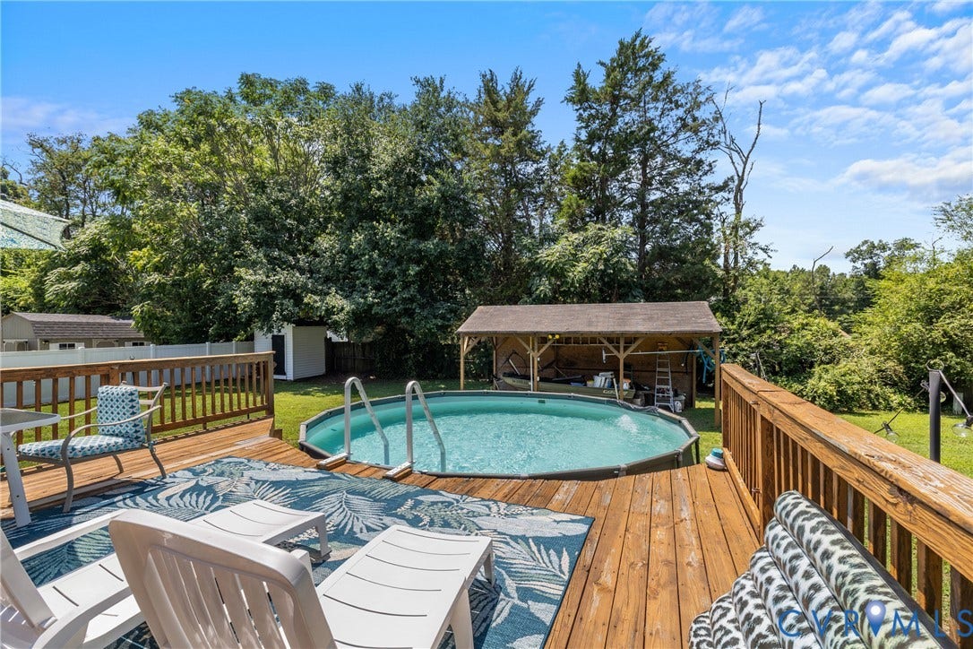 Expansive wood deck with an above-ground swimming pool, covered outdoor structure, manicured lawn, and mature trees